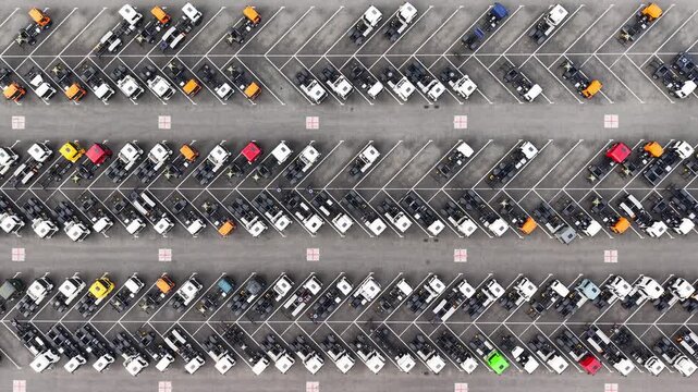 Aerial view of rows of parked new trucks and commercial vehicles in a large paved parking lot with colorful cabs and marked spaces. Drone footage of warehouse of manufactured lorry cars. Industrial co
