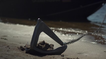 Small Boat Anchor on Chain Near Shore. Anchor Holds a Black Boat in Sunny Weather. Close-Up of the Anchor. © Vital9c