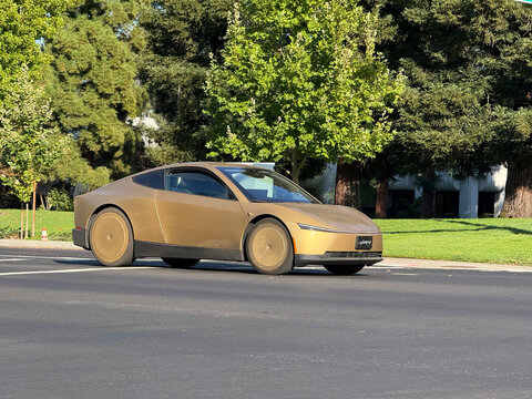 Gold Tesla Cybercab drives on a paved road bordered by grass and trees - Palo Alto, California, USA - October 8, 2026