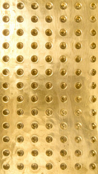A polished gold metal plate with a repeating tactile stud pattern creates a luxurious, industrial texture. Nobody present. This abstract, minimalist surface evokes prestige, symmetry, and depth.