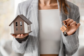 Real estate investment and home ownership, woman holding a model house and keys for mortgage loan...