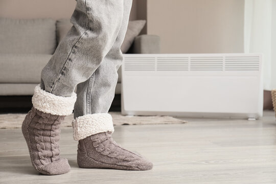 Cozy home comfort and winter warmth, person wearing soft knitted wool socks and jeans standing near a heater in a living room during cold weather