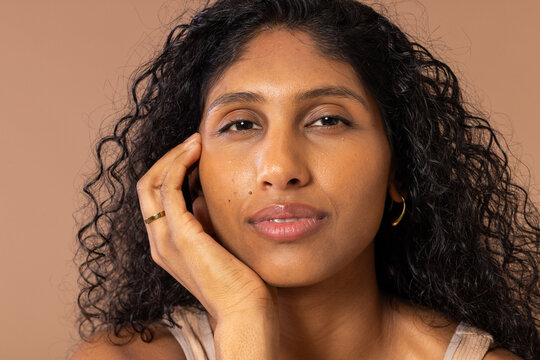 African American woman resting on left hand in studio, showing gold hoop, ring, glossed lips, tank