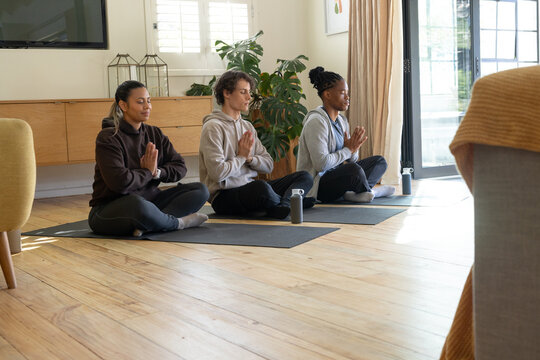 Diverse friends meditating on yoga mats at home wearing workout clothes with water bottles