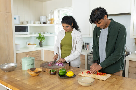 Indian couple slicing red onion, red pepper on kitchen island using two cutting boards, compost