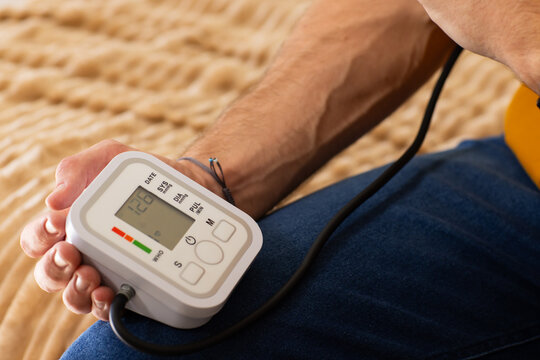 Man holding digital blood pressure monitor and checking cuff on right forearm on bed