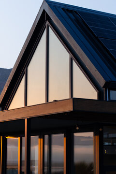 Modern triangular gable facade is bathing in warm sunrise light on coastal site