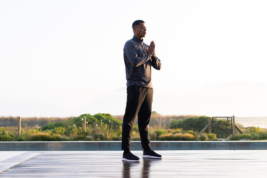 African man aged 20s in dark sportswear standing with palms pressed on reflective coastal deck
