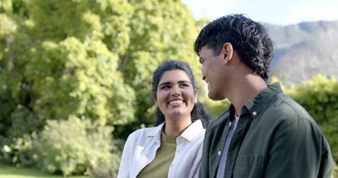 Asian couple sitting in garden woman smiling, causing man turning head, meeting gaze affectionately