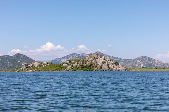 Scenic summer view of calm blue waters and rocky green islands at Lake Skadar in Bar municipality Montenegro with rugged mountains under a sunny clear sky on a bright peaceful day