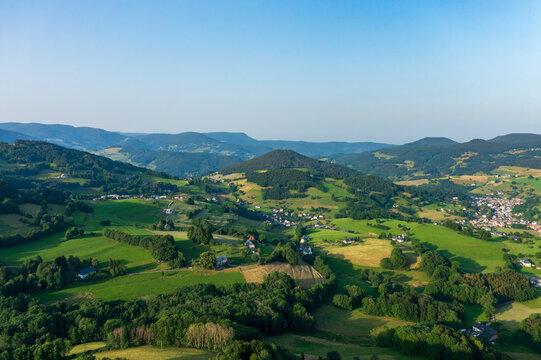 A wide aerial view shows green farmland, wooded hills and small villages under a clear blue sky in Alsace.
