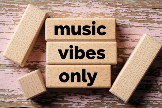 Wooden blocks with text music vibes lie on pink rustic wood surface. Creative typography message on timber cubes. Minimalist concept for audio lovers, lifestyle mood, sound enthusiasts. Aesthetic