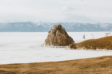 Scenic landscape of frozen Lake Baikal and rocky Shamanka Crag in Khuzhir, Irkutsk Oblast, Russia, showing tourists walking near icy shores against distant snowy mountain ranges © TravelFlow