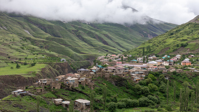 Scenic panorama of Magar village settled along rocky slopes and verdant valleys in Dagestan Russia with low clouds covering the majestic Caucasus mountain peaks on a cloudy summer day