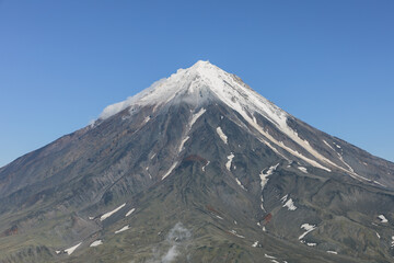 Majestic view of Koryaksky stratovolcano with snow covered slopes and rocky volcanic terrain under a clear blue sky in Kamchatka Krai, Russia, showcasing wild subarctic nature © TravelFlow