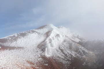 Scenic view of the snow covered volcanic ridge of Avachinsky volcano surrounded by fog and clouds in Kamchatka Krai, Russia, showcasing rocky terrain and dramatic wilderness © TravelFlow