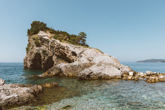 Scenic view of the layered coastal cliff and turquoise adriatic sea near Budva municipality in Montenegro, displaying natural limestone formations along the summer shore