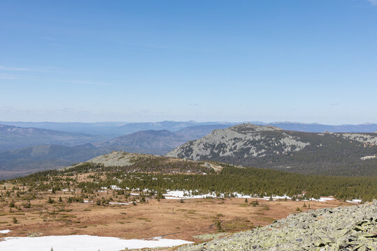 Scenic panoramic view of alpine tundra and taiga forest from Mount Bolshoy Iremel in the Republic of Bashkortostan, Russia, featuring rocky slopes and distant ranges under clear blue sky