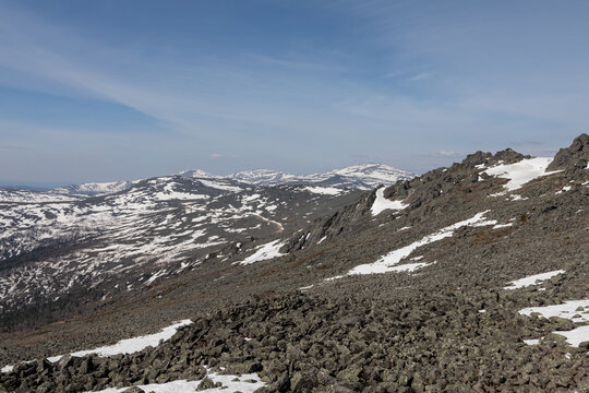 Panoramic view of rugged rocky slopes and snow patches on Mount Konzhakovsky Kamen under a clear blue sky in Sverdlovsk Oblast, Russia during bright spring season
