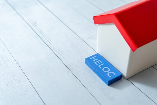 Miniature white house and a blue block with text HELOC. Home equity lines of credit and real estate finance concept. Copy space for text.