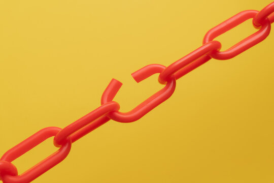 A red chain with a broken link on a yellow background. Supply chain disruption, breaches, weakness, risk, and system breakdown concept.