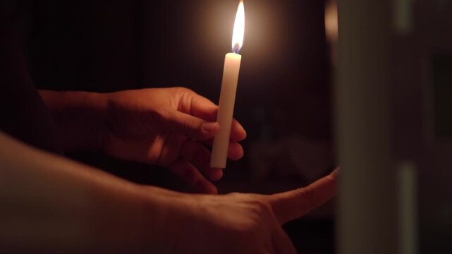 A woman holds a candle in a dim room and trying to turn on switch. electricity crisis concept.