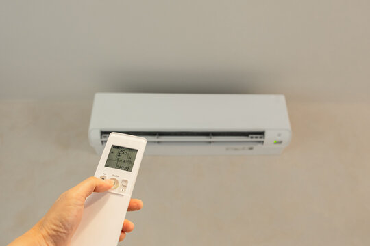 Hand of humau  holding a remote control to adjust the temperature of a wall mounted air conditioner in a room, representing home comfort, climate control, and daily life convenience.concept home