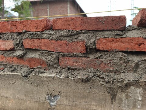 Red brick masonry wall laying on concrete foundation with cement mortar at building construction site, perfect for house structure progress, civil engineering, and masonry texture photo