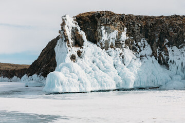 Majestic rocky cliff covered with thick winter ice and frozen splash formations rises above the snow surface on Lake Baikal in Irkutsk Oblast, offering scenic views across Russia © TravelFlow