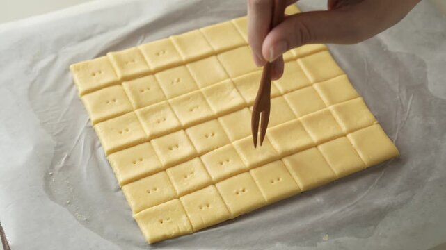Docking cheese cracker dough squares by poking holes with a small fork on parchment paper