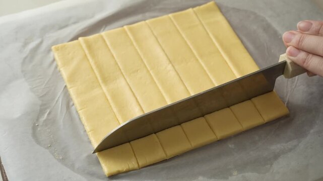 Cutting rolled cheese cracker dough into small squares with a large knife on parchment paper