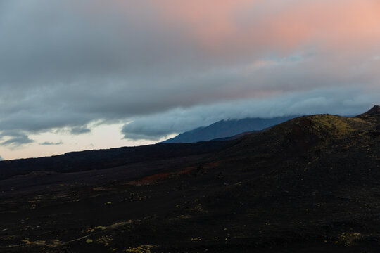 Dramatic evening landscape shows black volcanic slag fields and hills under cloudy pink sky across Tolbachik plateau in Kamchatka Krai, Russia, revealing wild deserted nature