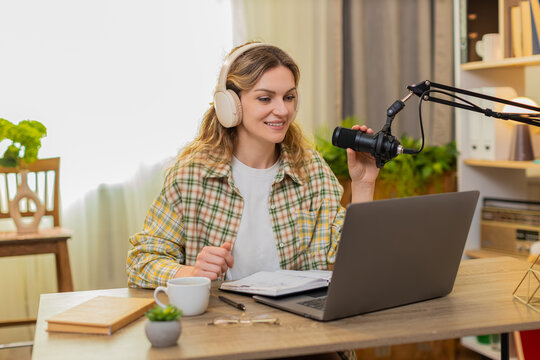 Young woman on home table records lesson with studio microphone and checks notes while explaining topic on laptop. Adult girl on home table speaks with confidence for podcast training in living room.