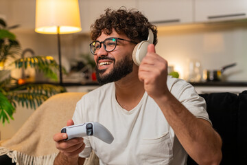 Arabian man at home plays on game console holds joystick leans forward enjoys play sees level score high. Egyptian guy on sofa cheers after win presses buttons shoots jumps feels thrill night victory. © Andrii Iemelianenko