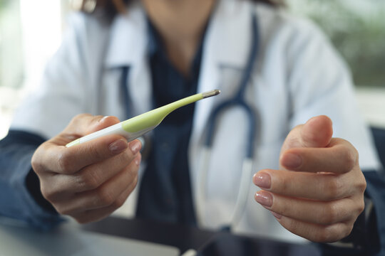 Doctor holding digital thermometer during medical checkup in clinic.