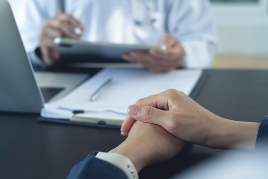 Female patient listening to doctor during consultation in clinic office with tablet and medical documents.