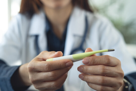 Close up of female doctor holding digital thermometer during medical checkup in clinic.