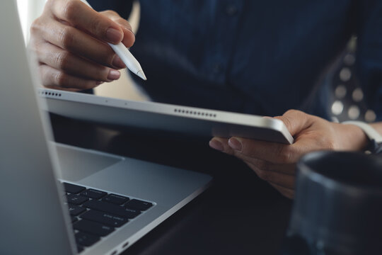Close-up of businesswoman using stylus on tablet beside laptop in office workspace, digital technology, online work concept.