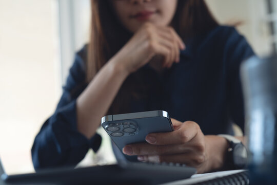 Close-up of business woman using smartphone while working at desk with laptop, modern business lifestyle concept.