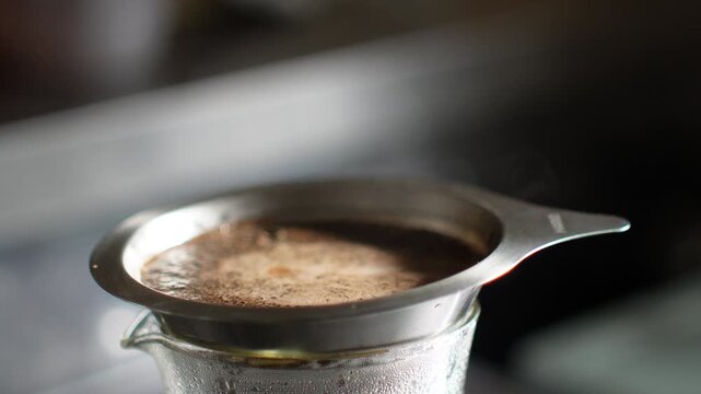 Close up of coffee grounds blooming in a stainless steel dripper as hot water is poured from a gooseneck kettle. Foam and bubbles rise on the surface, pour over coffee brewing, real time 4K.