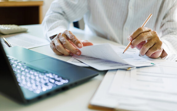 close up shot, asian businessman reviewing document at office working on laptop. professional lawyer reading and checking business documents and contract before giving advice to customers