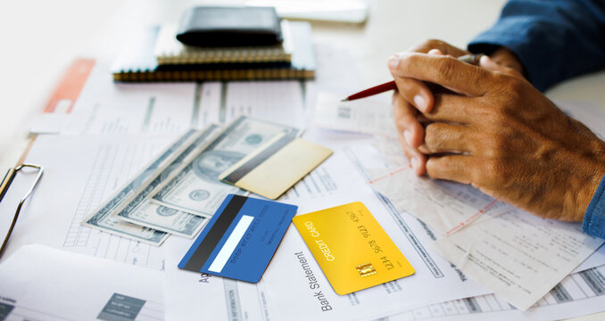 close-up shot, credit card with bank statement, dollor and many expense from credit card on table and hand of the man holding pen worry about debt