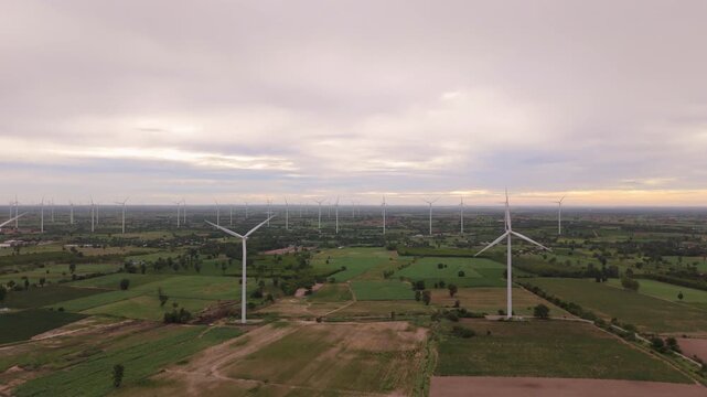 Drone view of wind turbine over farmland under cloudy dawn sky for green energy