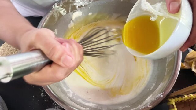 Pouring melted butter or oil into a mixing bowl containing the flour and water mixture while stirring the ingredients in preparation for frying.