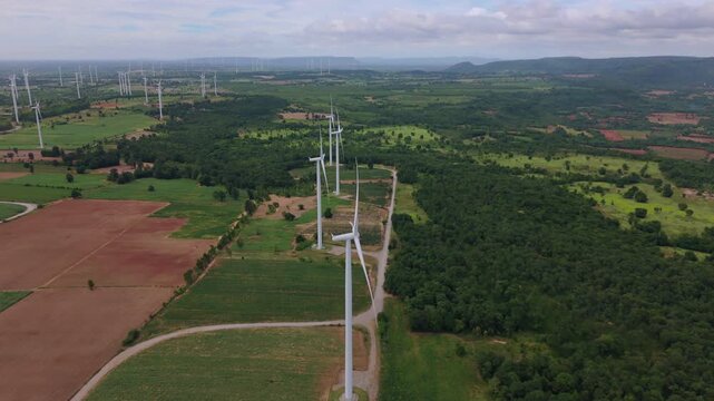 Aerial view of wind turbine row on rural road through green forest and farmland