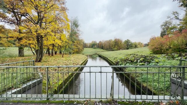 POV walkthrough of an empty bridge in Pavlovsk Park, Russia, shot on stabilizer in slow motion. Smooth forward camera motion moves over a calm river surrounded by rainy autumn trees.