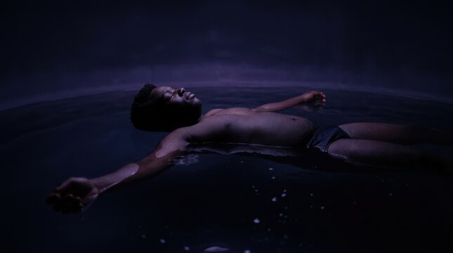 A man floating peacefully in dark water during a sensory deprivation tank therapy session