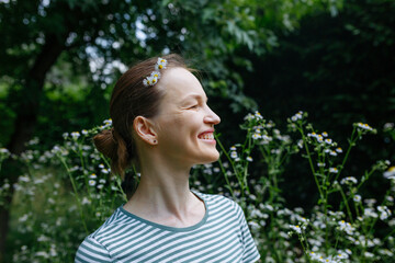 Smiling Woman with Daisies in Her Hair Enjoying Nature in a Garden © Victoria