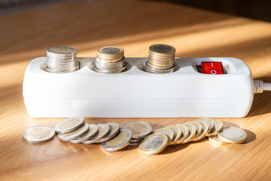 Euro coins filling a power strip, with additional coins on the table, illustrating the financial cost of electricity consumption and the potential for energy saving by switching off devices