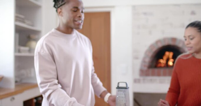 Diverse pals man pointing to grater woman rust sweater grating cheese at kitchen island making meal